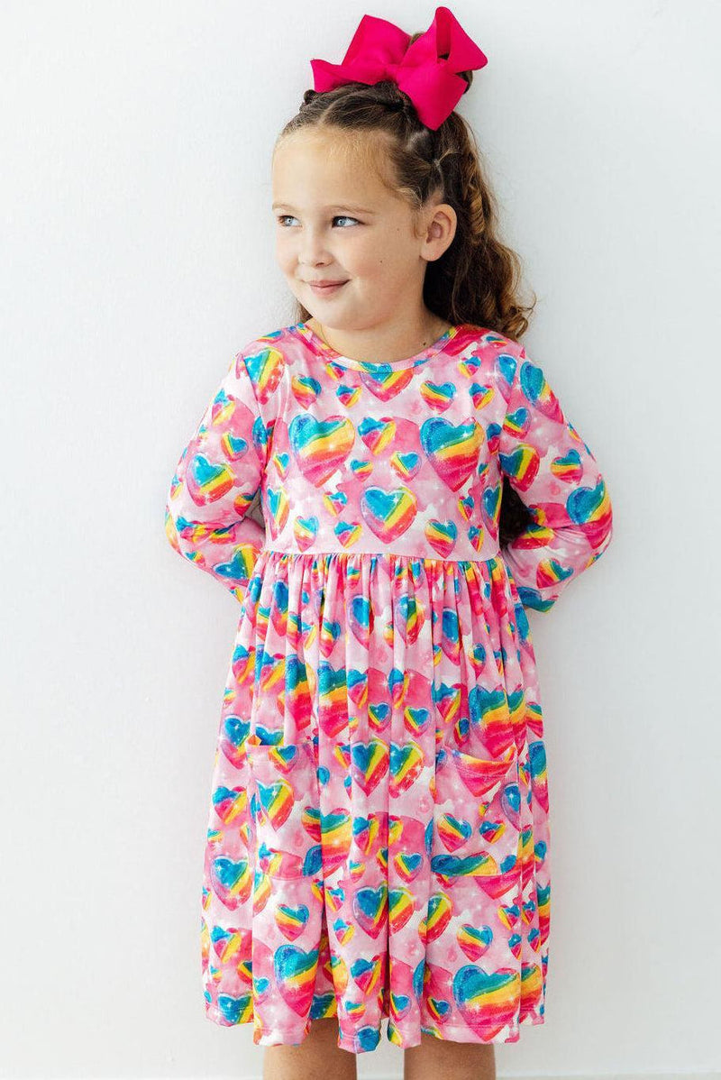 Girl wearing Sugar & Spice 3/4 Sleeve Pocket Twirl Dress with rainbow hearts on pink, full twirl skirt