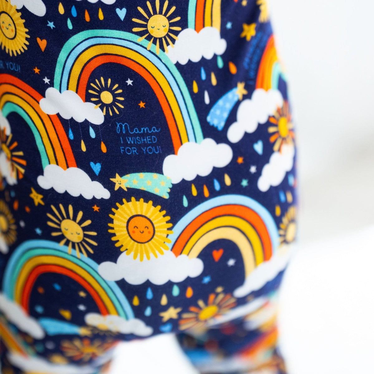The Second-Skin Convertible Romper Here Comes the Sunshine (Blue) with rainbow, sun, and cloud print.