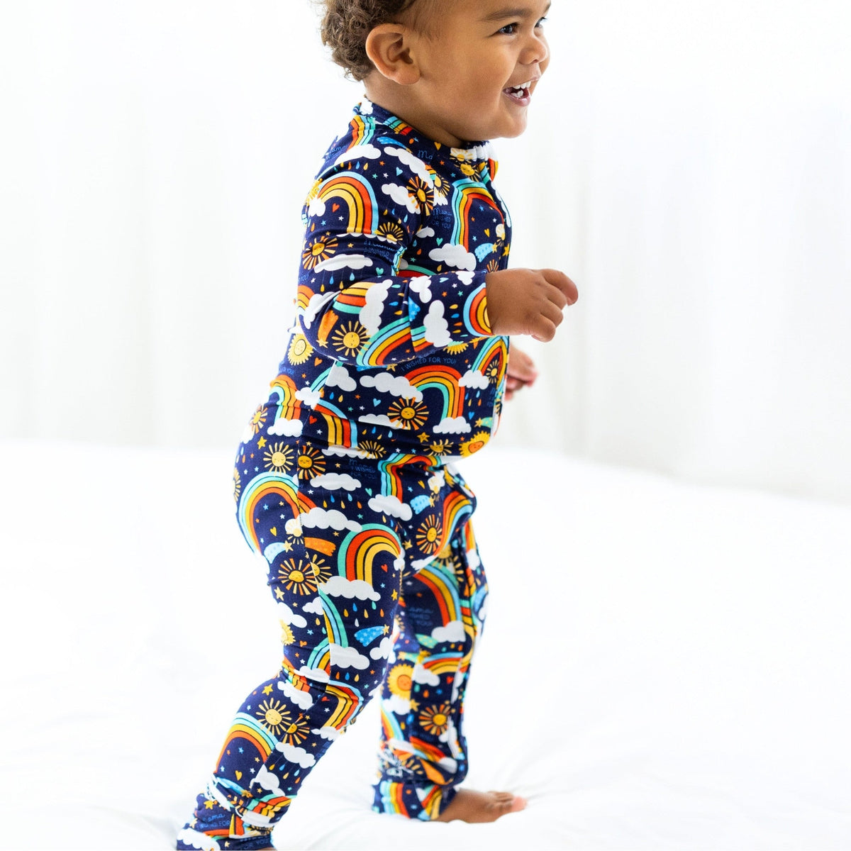 Child wearing The Second-Skin Convertible Romper, Here Comes the Sunshine Blue, rainbow and cloud print.