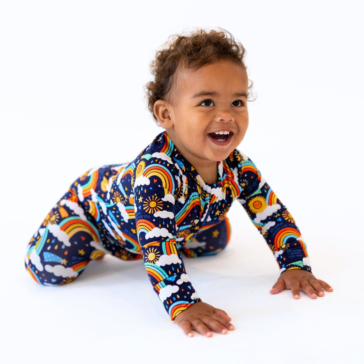 Baby in a blue Second-Skin Convertible Romper with rainbow sun print, smiling.