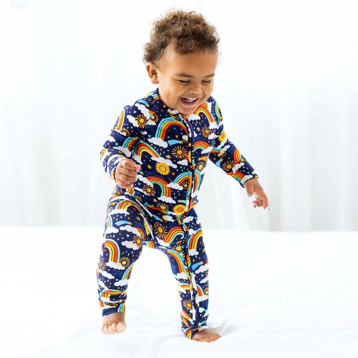 Here Comes the Sunshine blue Second-Skin Convertible Romper with rainbow sun print on a laughing toddler.