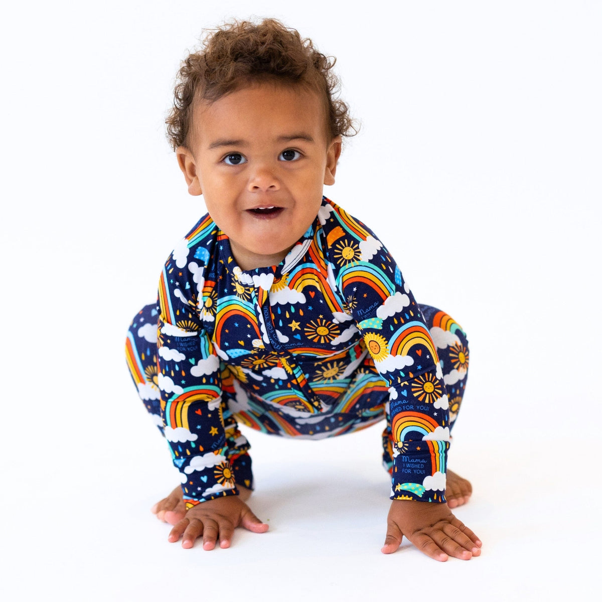 Baby wearing The Second-Skin Convertible Romper in Here Comes the Sunshine Blue, zippered sun, rainbow, clouds print.