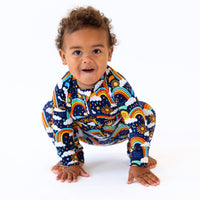 Baby wearing The Second-Skin Convertible Romper in Here Comes the Sunshine Blue, zippered sun, rainbow, clouds print.