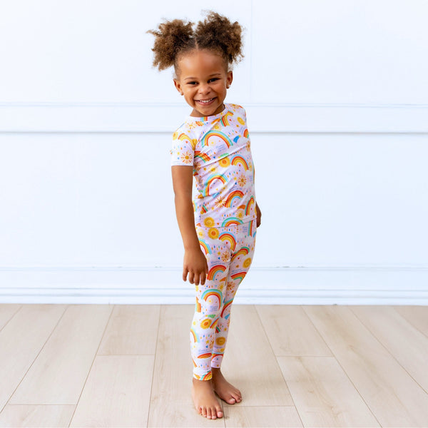 Child wearing pink Here Comes the Sunshine Second-Skin 2-Piece short-sleeve pajama with sun and rainbow print.