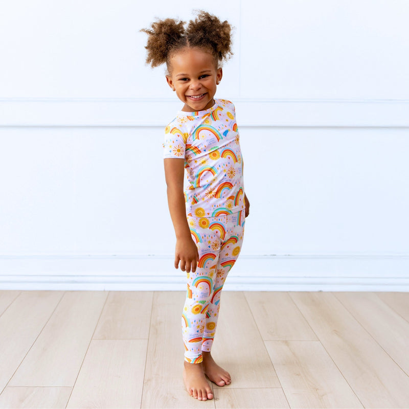Child wearing pink Here Comes the Sunshine Second-Skin 2-Piece short-sleeve pajama with sun and rainbow print.