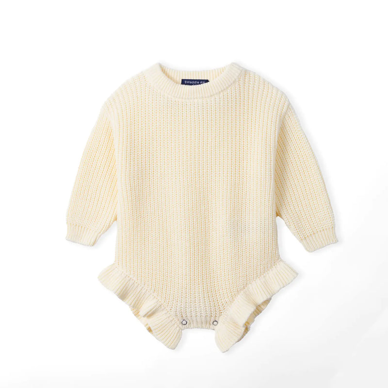 Cream chunky knit baby romper flat lay with ribbed cuffs, crew neck, and ruffled leg openings secured by metal snaps