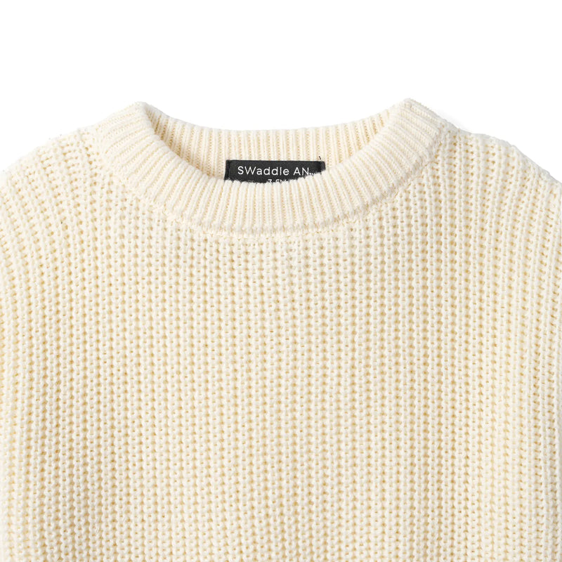 Close-up of cream ribbed knit texture and black Swaddle AN brand label inside the crew neckline