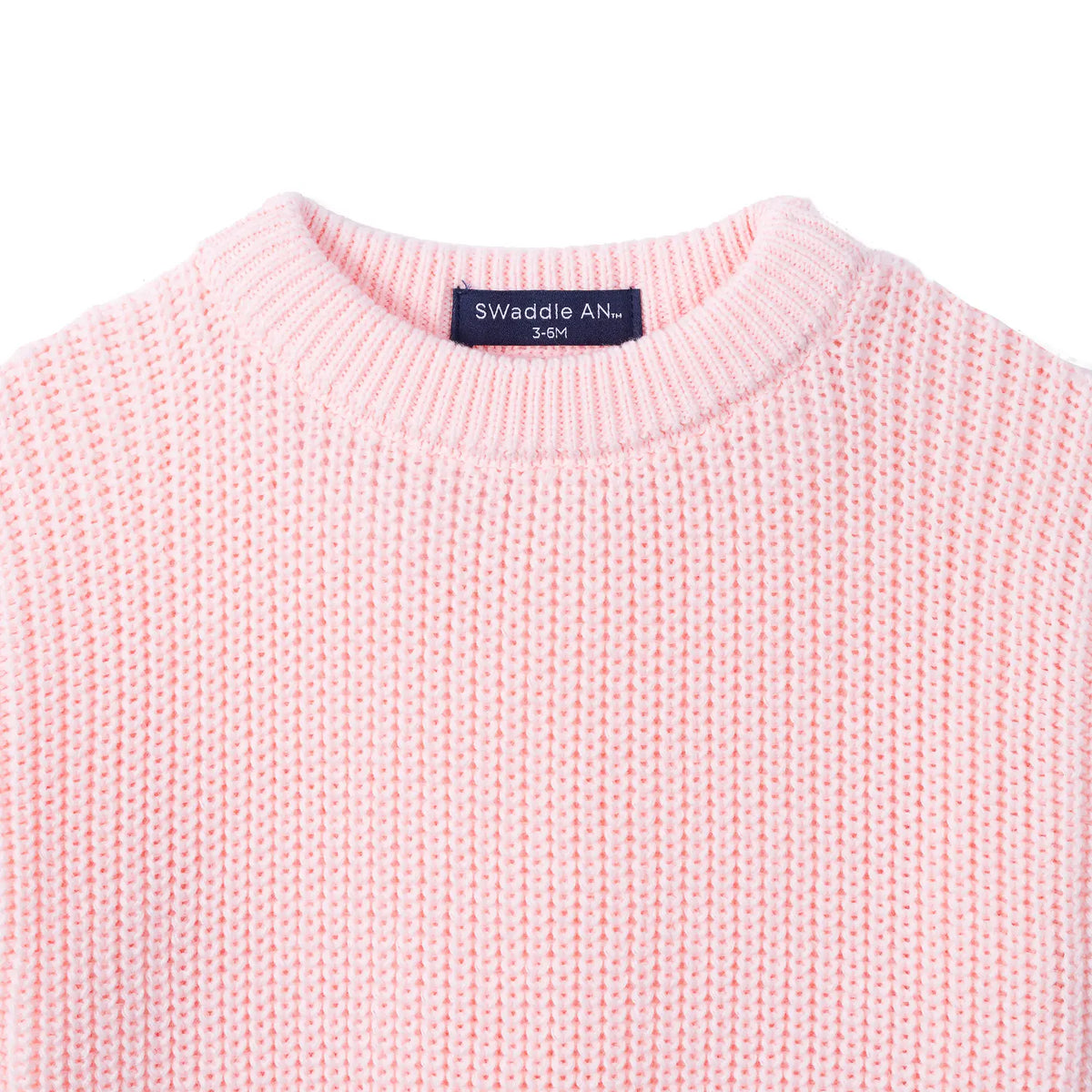 Close-up of pink chunky knit texture and navy label reading SWaddle AN 3-6M inside collar