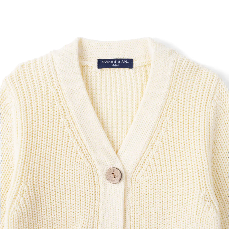 Close-up of cream baby cardigan neckline showing ribbed trim, wooden button, and navy Swaddle AN label