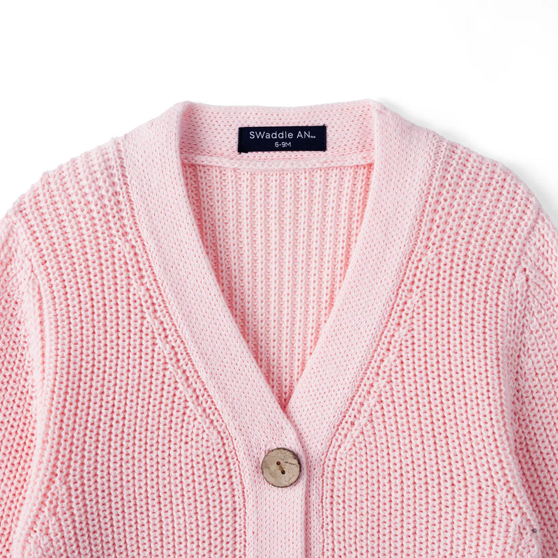 Close-up of light pink knit texture, V-neck collar, top wooden button, and black SWaddle AN size label