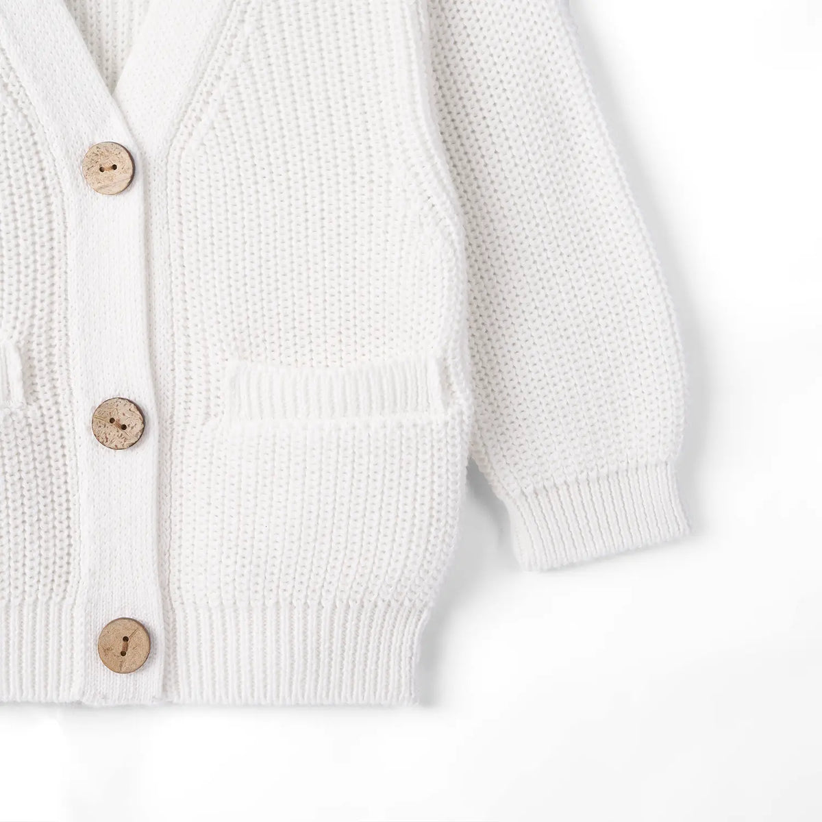Side view of white cardigan pocket detail, ribbed cuff, and aligned wooden buttons on placket