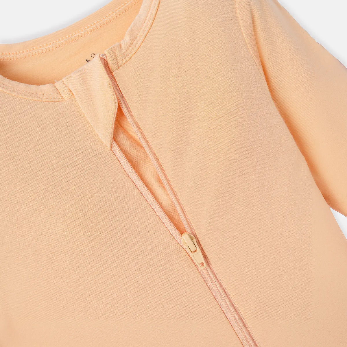 Extreme close-up of two-way zipper mechanism and reinforced tape on peach infant sleepwear