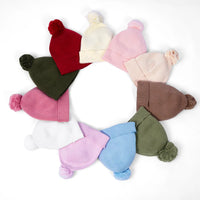Assorted colors of knit baby beanies with ribbed cuffs and pom-poms arranged in circle