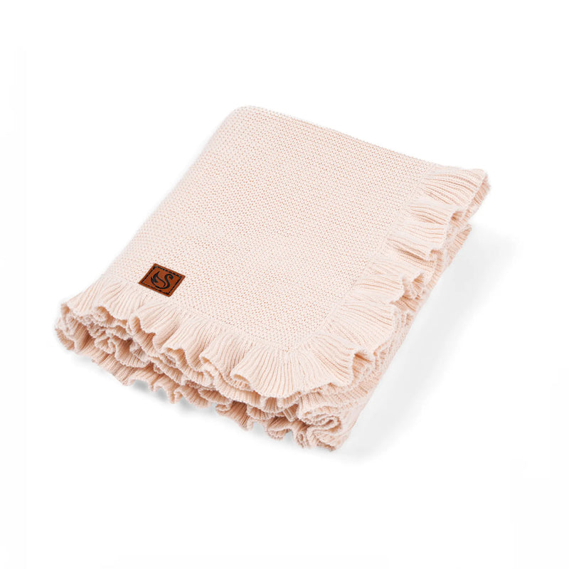 Folded pale pink garter stitch baby blanket with ruffled edge and brown brand tag on white background