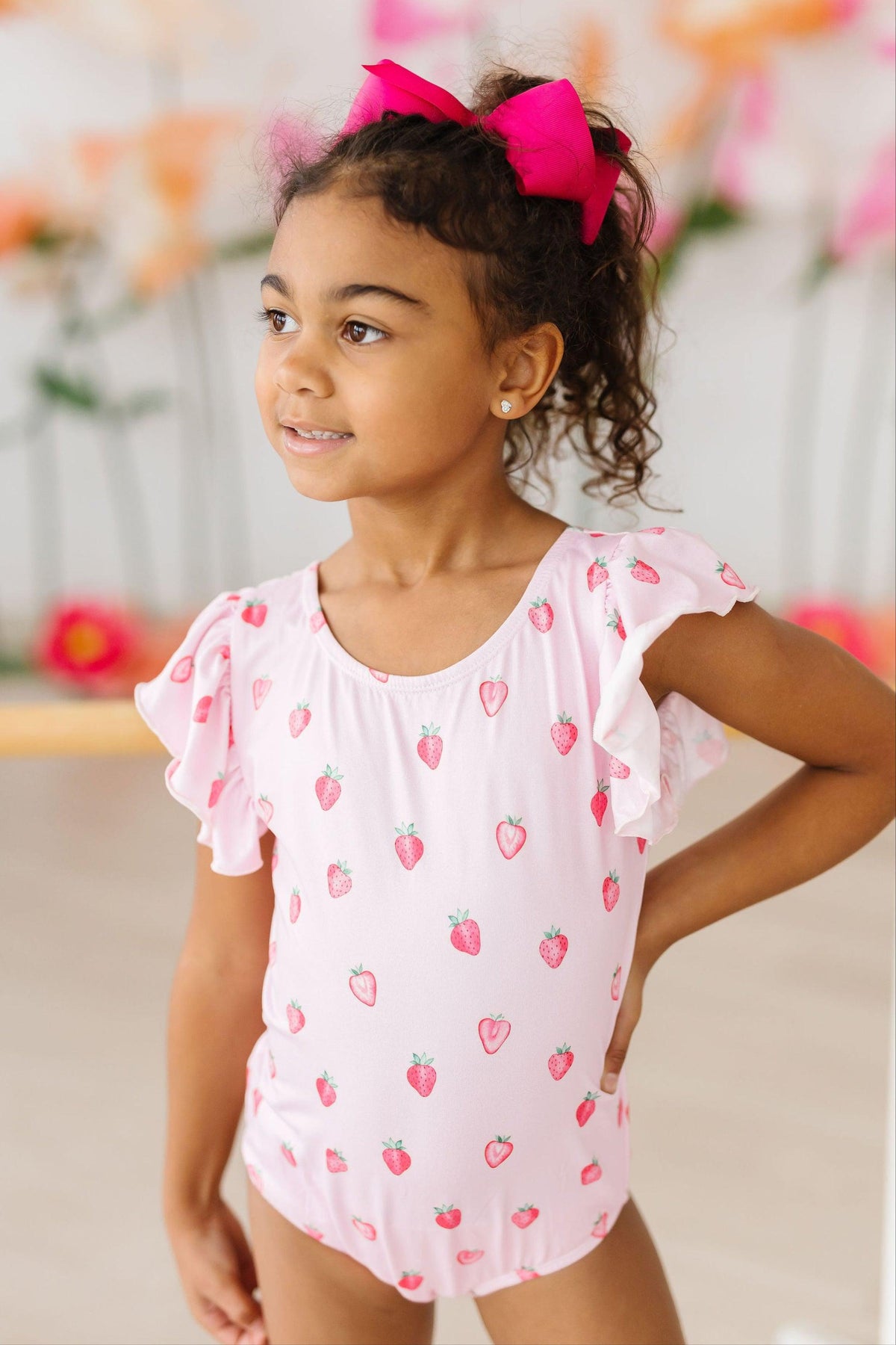 Sweet Strawberries short-sleeve flutter-sleeve leotard worn by a young girl with a pink bow in her hair.