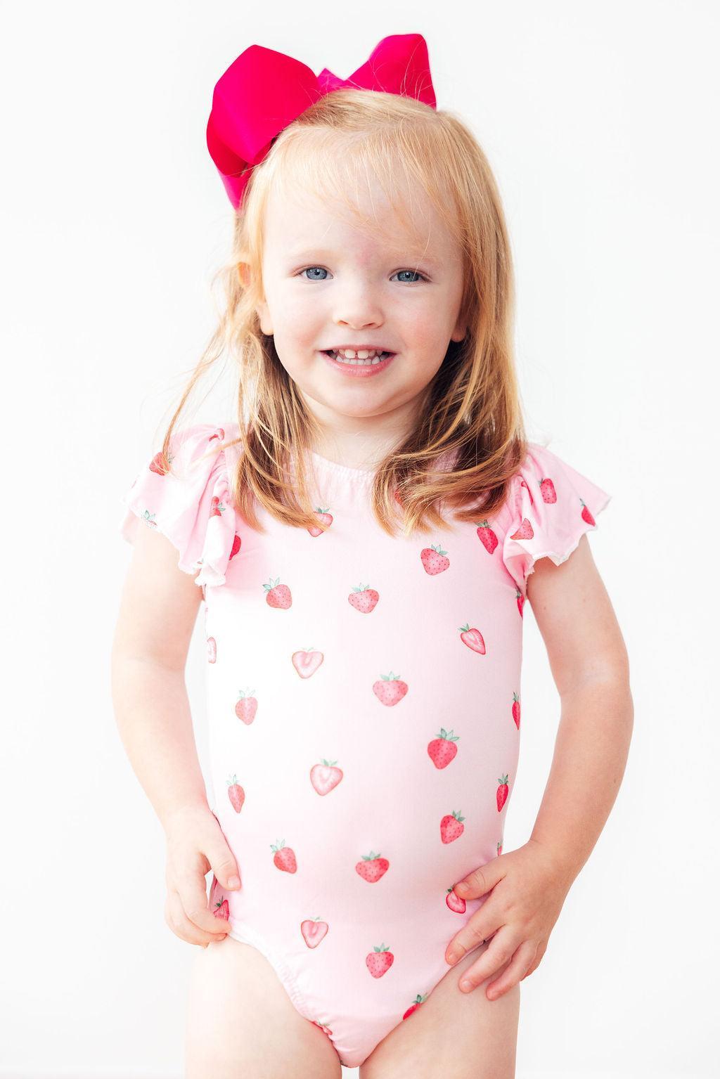 Toddler girl in Sweet Strawberries short-sleeve flutter-sleeve leotard with a bright pink bow.