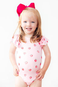 Toddler girl in Sweet Strawberries short-sleeve flutter-sleeve leotard with a bright pink bow.