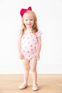 Sweet Strawberries short sleeve flutter sleeve leotard on a smiling toddler girl with a pink bow.
