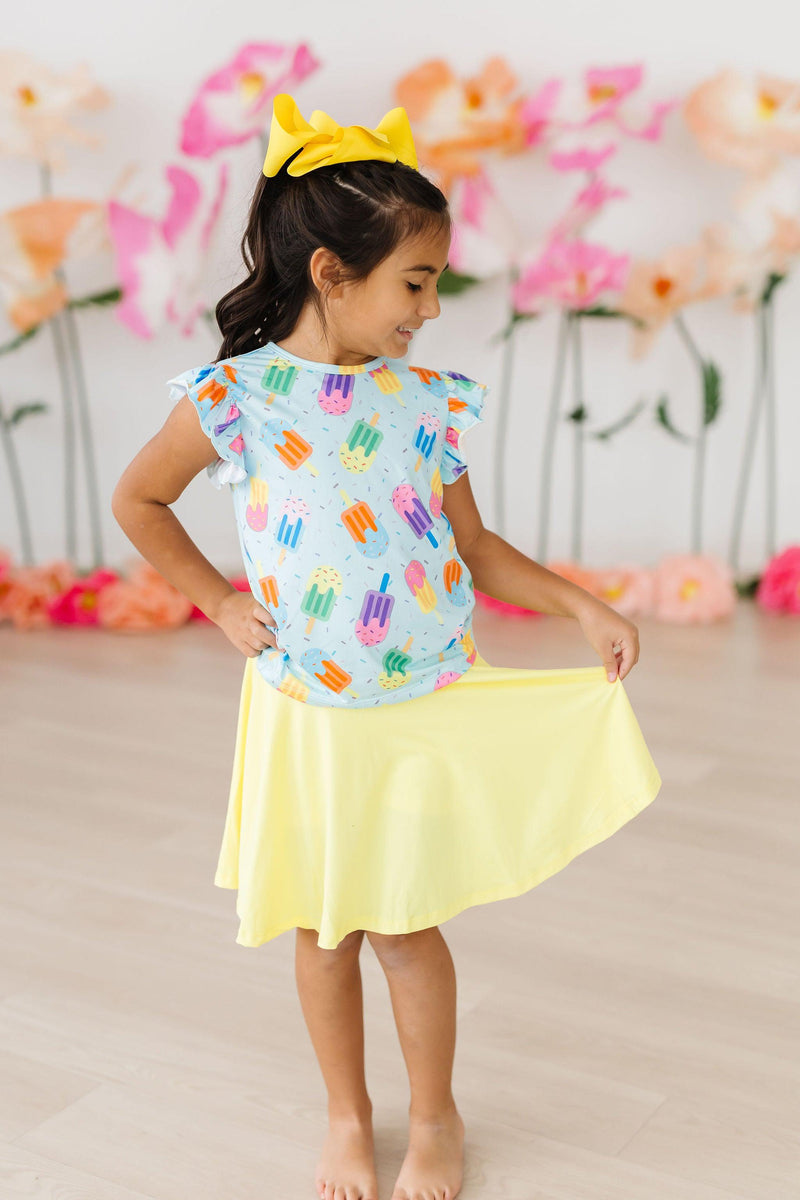 Smiling girl in the Adorable 'Sweet Treat' Ruffle Sleeve Tee and yellow skirt, demonstrating versatility and playful fashion.