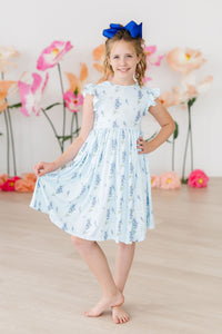 Texas Bluebonnets Flutter Sleeve Twirl Dress for Girls, light blue floral print worn by smiling girl with a blue bow.