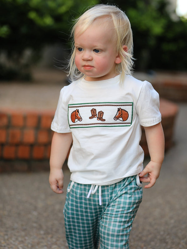 Young boy in white T-shirt with horse and cowboy boot embroidery, mint plaid drawstring pants.