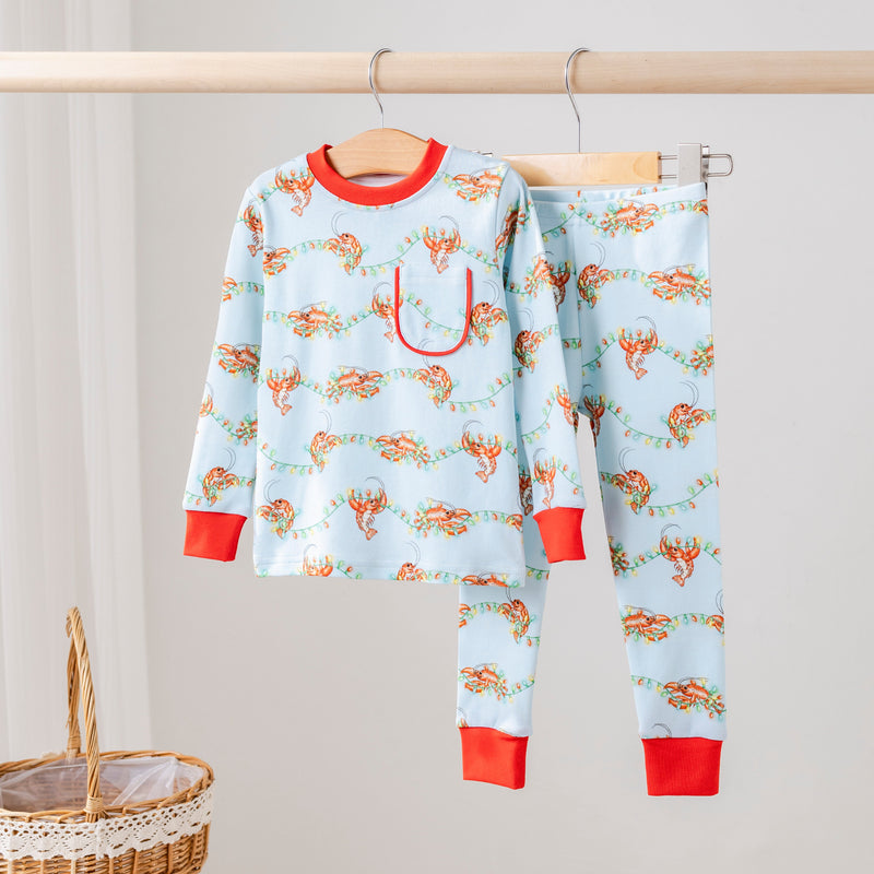 Twinkling Tails Organic Cotton Kids Pajamas in light blue with crawfish tangled in Christmas lights and red cuffs.