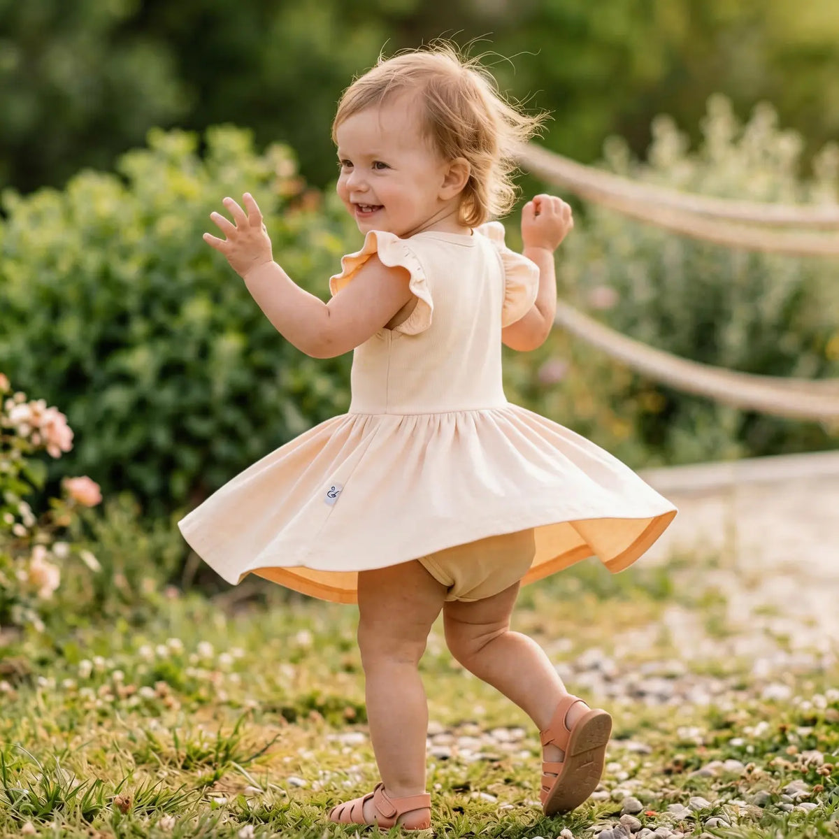 Toddler running in garden wearing sand bamboo twirl bodysuit dress with flowy skirt movement