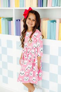 Smiling girl in a Unicorn Kitties 3/4 sleeve twirl dress with pockets and a red bow.