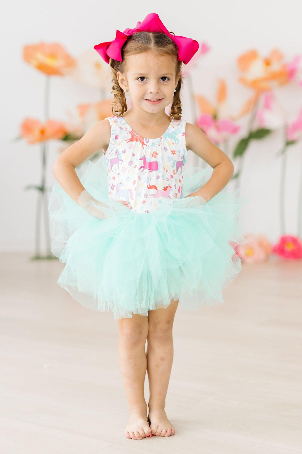 Little girl wearing Unicorn Wish Tank Tutu Leotard with a fluffy mint green tutu and a bright pink bow, ready to dance.