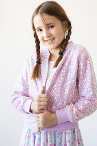 Smiling girl wearing lavender sequin jacket with braided pigtails.