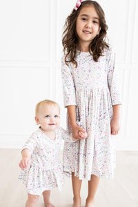 Two sisters wearing One in a Million 3/4 sleeve twirl dresses with pastel heart print, indoors.
