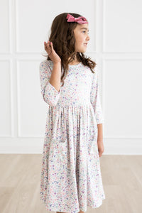 Little girl in pastel heart-print twirl dress with 3/4 sleeves, full skirt, and pink bow.
