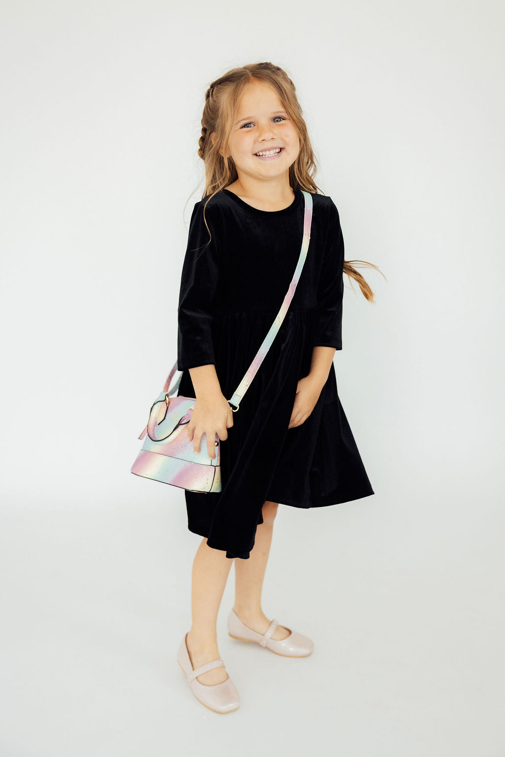 Smiling girl in black dress wearing iridescent unicorn glitter crossbody purse with long strap. Perfect fashion accessory.