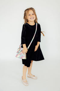 Smiling girl in black dress wearing iridescent unicorn glitter crossbody purse with long strap. Perfect fashion accessory.