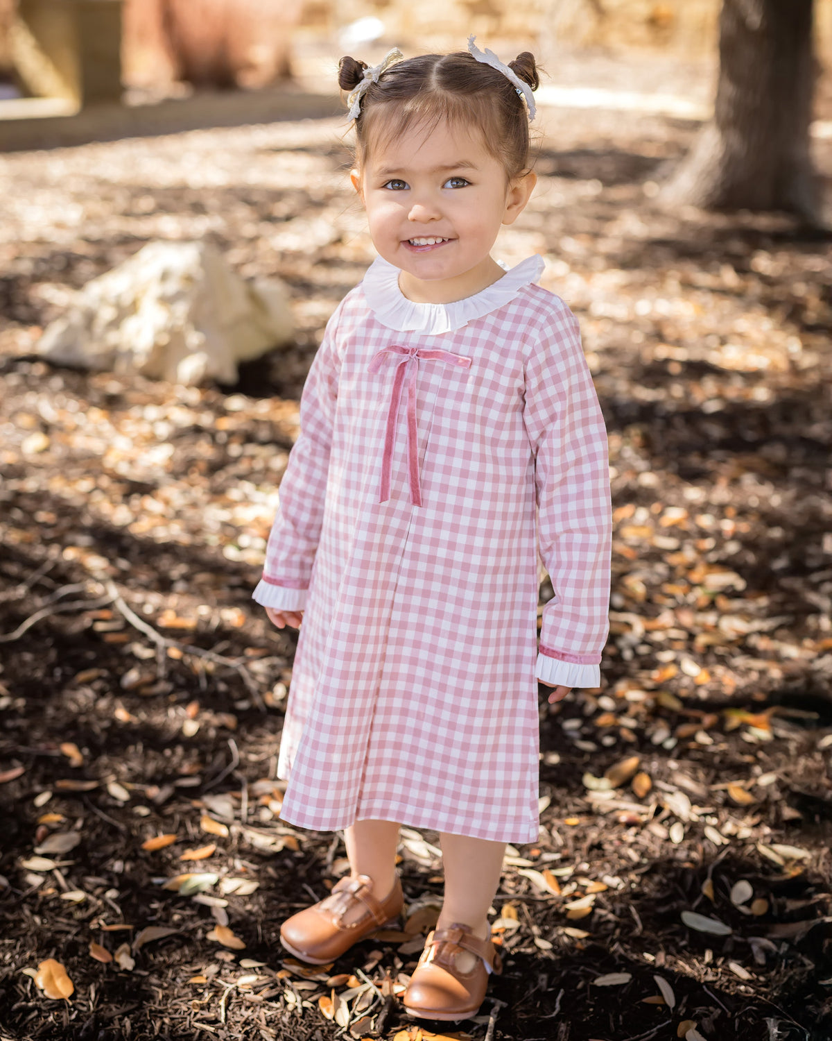 Girl wearing pink gingham A-line dress with white ruffled collar, darker rose velvet bow at chest, and ruffled cuffs.