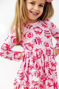 Girl wearing Vintage Cakes Long Sleeve Pocket Twirl Dress in pink cake-print fabric with a pocket.