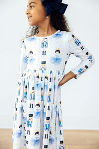 Young girl in a long sleeve pocket twirl dress with nutcracker and ballerina print and navy bow.