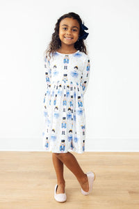 Girl in long sleeve twirl dress with nutcracker and ballet dancer print, full circle skirt, front pocket, and white sparkly shoes.