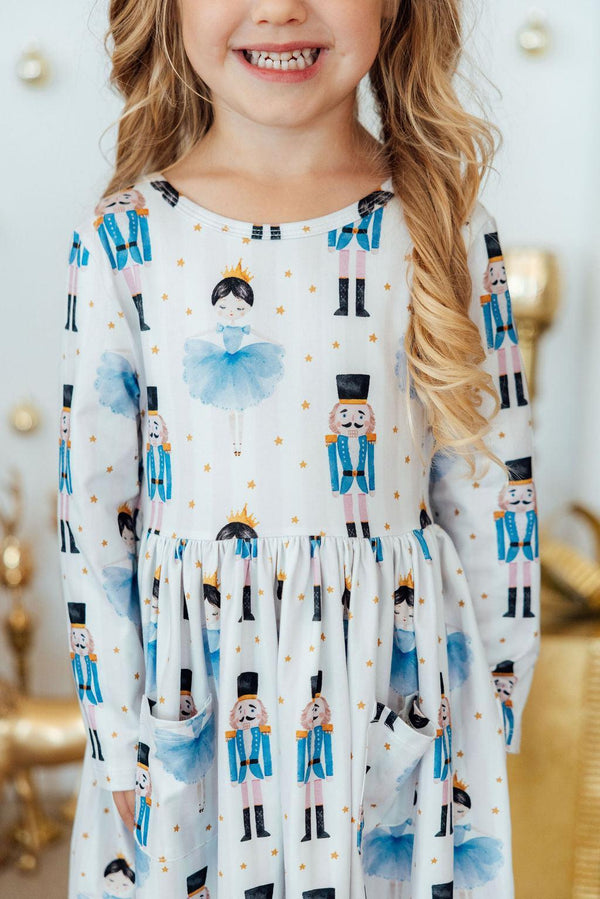 White long sleeve twirl dress featuring blue ballerina, nutcracker, and star print with front pockets.