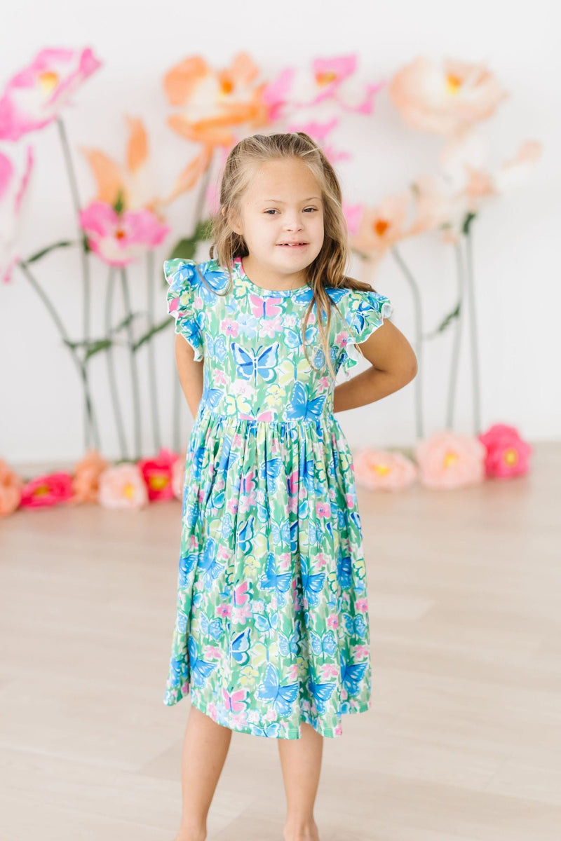 Girl smiling in the Watercolor Butterflies Flutter Sleeve Twirl Dress, highlighting its playful flutter sleeves and bright watercolor butterfly pattern.
