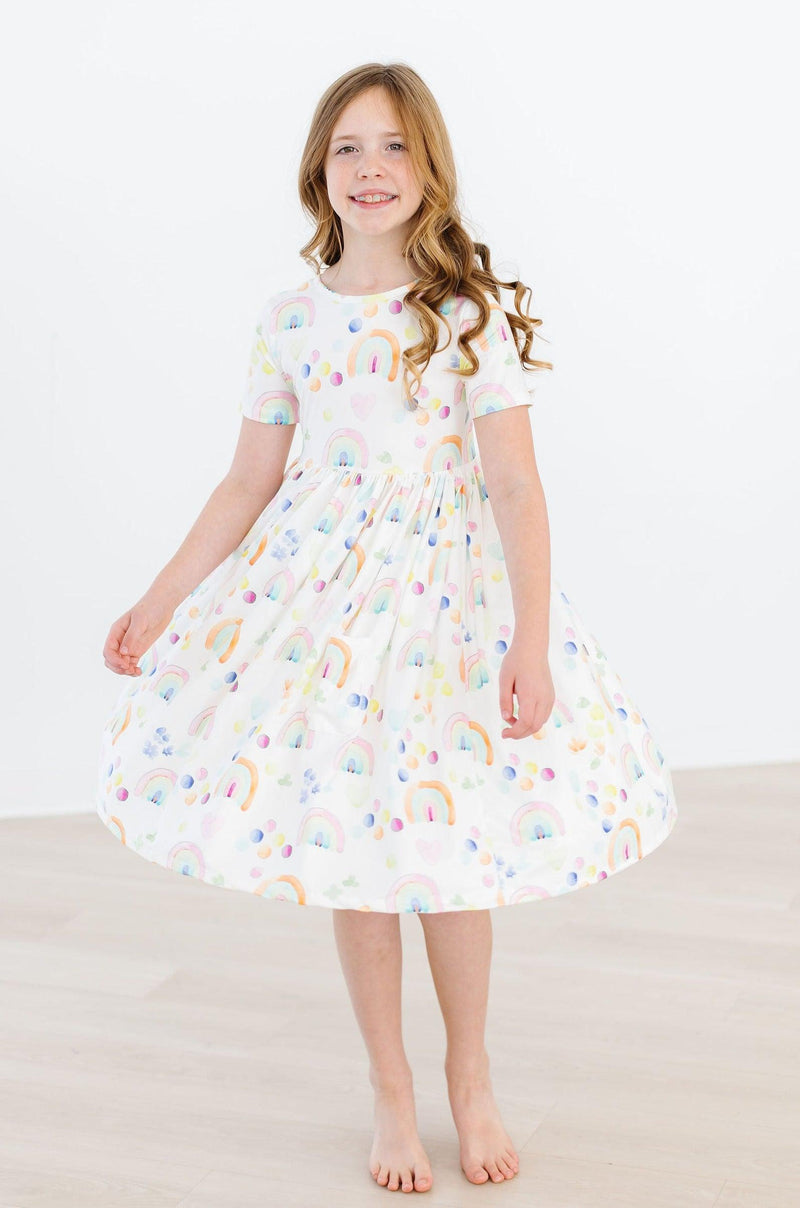 Cheerful girl twirling in the Watercolor Rainbows S/S Pocket Twirl Dress from Mila & Rose, highlight the full skirt and colorful design.