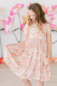 Girl twirling a pink and white floral short sleeve pocket dress with a gathered skirt against a floral backdrop.