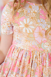 Girls short sleeve pocket twirl dress with pink, purple, and gold floral print and gathered skirt for school or play.