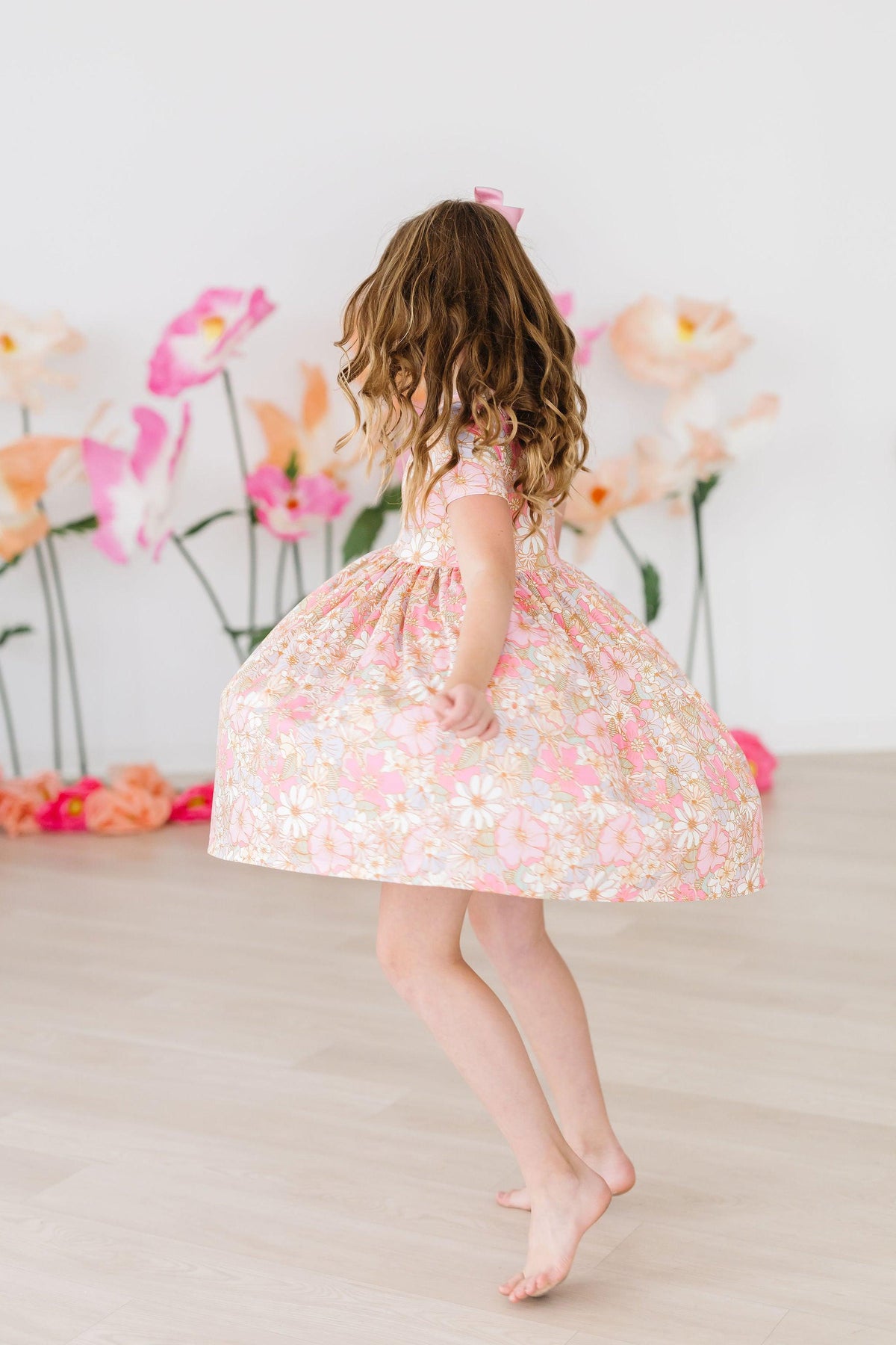 Toddler twirling in pink floral short sleeve pocket dress with scoop back, designed for comfort and easy wear.