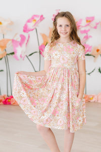 Girl twirling in pink floral short sleeve pocket dress with scoop back, perfect for school and play.
