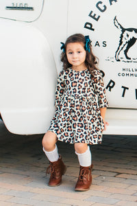 Toddler girl wearing a leopard print 3/4 sleeve twirl dress with pockets, styled with brown boots and leg warmers.
