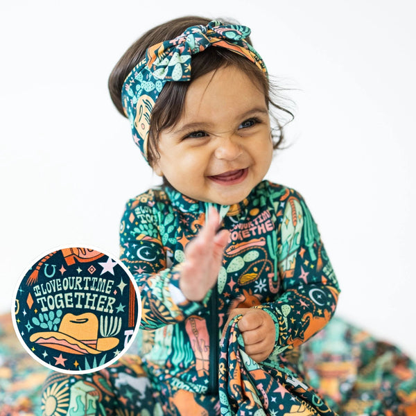 The SoftKnot Bow | Wild West bamboo headwrap on a smiling toddler in a colorful print.
