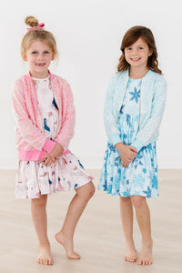 Two young girls wearing matching dresses and cardigans on a plain background