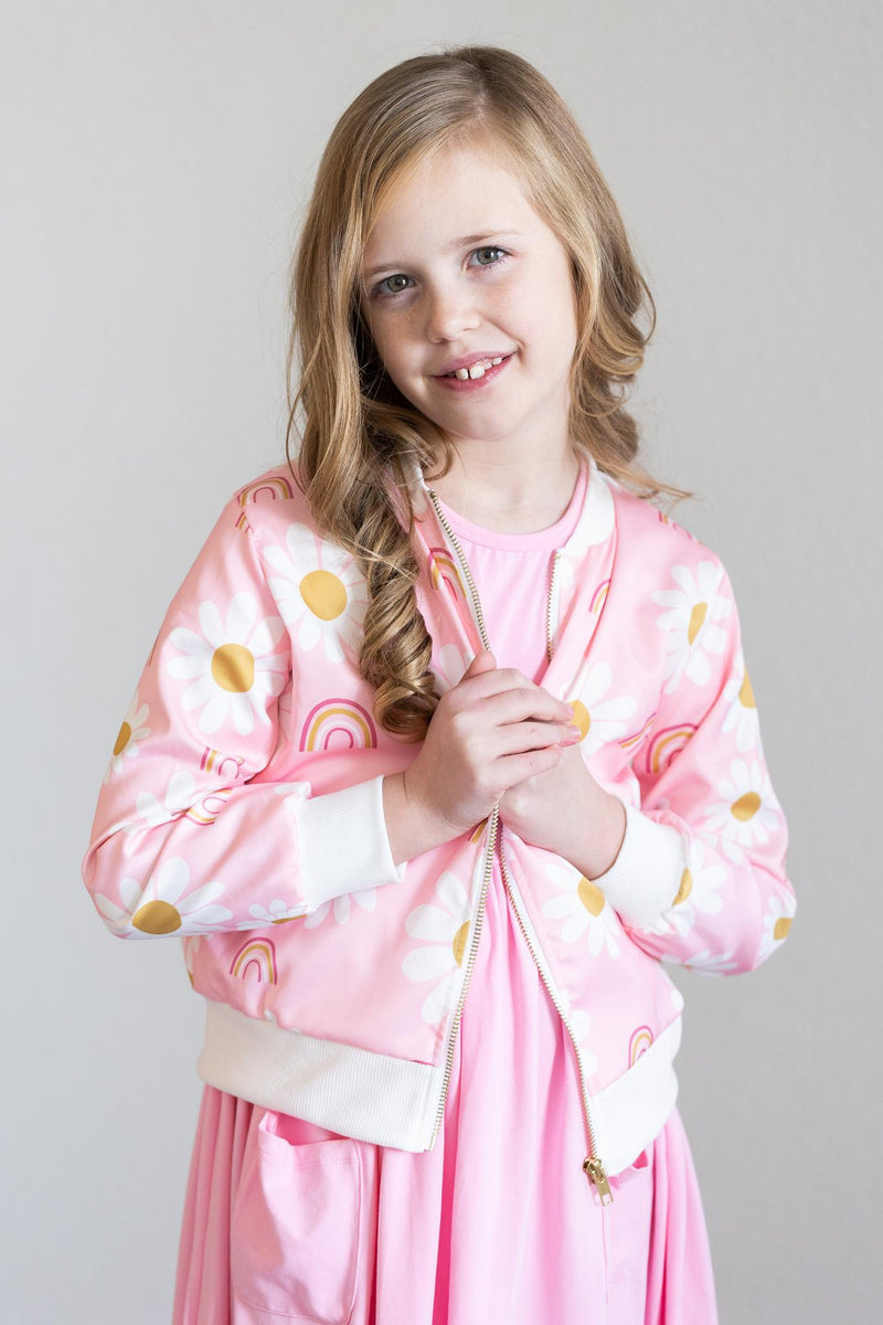 Smiling girl wearing the You are My Sunshine Satin Jacket, a stylish pink jacket adorned with daisies, perfect for adding flair to any outfit.