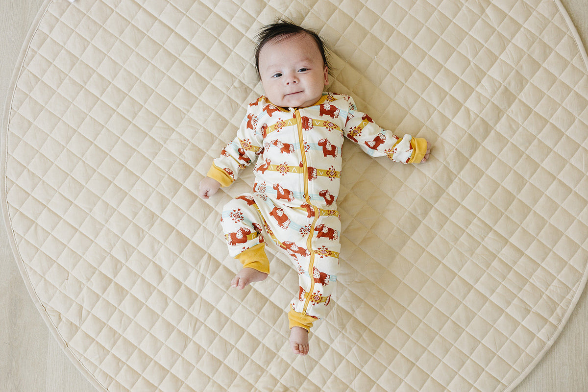 Baby wearing GOTS certified organic cotton zip romper with Aztec pony print, lying on quilted mat. Chemical-free safety.